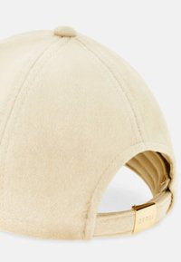 Casquette de baseball beige avec une finition douce et texturée, dotée d'un dessus arrondi et d'une sangle réglable avec un détail en métal doré.