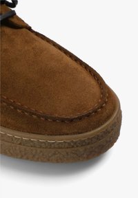 Brun ruskindsko med en rund tå, syet detailing og en tekstureret gummisål med et lagdelt design.