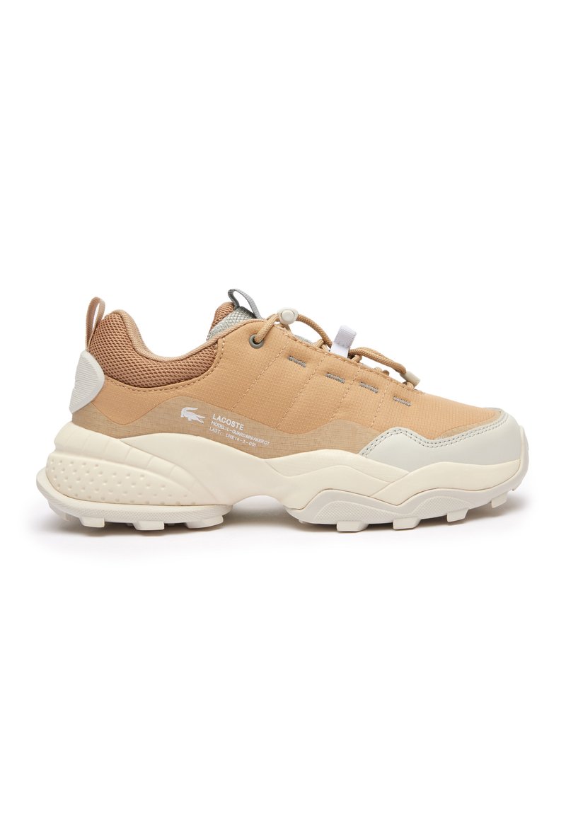 Sneakers Lacoste w jasnym brązie i kremie, z teksturowanym materiałem, grubą podeszwą i elastycznymi sznurowadłami zapewniającymi pewne dopasowanie.