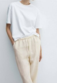 Bílý bavlněný tričko s krátkým rukávem spárované s světle béžovými lněnými kalhotami s elastickým pasem a stahovací šňůrkou se korálky.