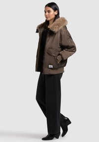 Brown padded jacket with a faux fur collar, featuring zippered pockets and ribbed cuffs, paired with black wide-leg trousers and heeled boots.