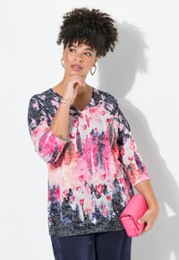 Färgstark topp med abstrakt mönster, V-ringning och trekvartslånga ärmar; i nyanser av rosa, svart och subtila texturer.
