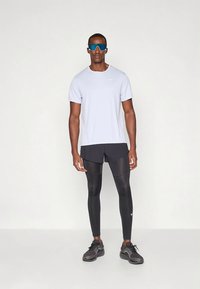 Vaaleanharmaa lyhythihainen urheilupaita, mustat shortsit, mustat kompressiotrikoat ja harmaat juoksukengät; päällä siniset heijastavat aurinkolasit.