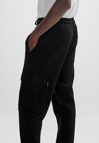 Svarta joggerbyxor av mjukt material, med sidfickor, en cargoficka med knappstängning och ett elastiskt midjeband.