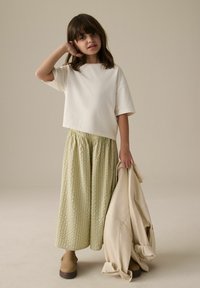 Vit kortärmad t-shirt, grönrandig fladdrande kjol, bruna skor och beige jacka. Slät tyg, avslappnad passform och rynkad midja.