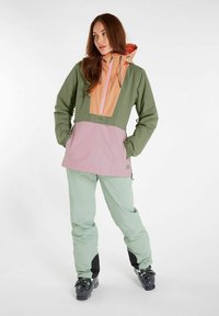 Kleurgeblokte waterdichte jas in groen, roze en oranje met een voorste half-rits, verstelbare capuchon en zijzakken; gecombineerd met mintgroene broek.