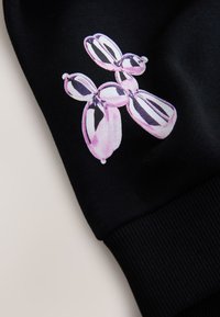 Tessuto nero con polsino a costine, con un design di palloncini lucidi rosa e bianchi con ombreggiature e riflessi sulla manica.