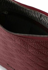 Bolso de cuero texturizado burdeos con una cremallera plateada, con un forro interior a rayas. Apto para objetos pequeños.