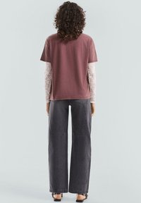 Rdzawy różowy bawełniany t-shirt z krótkim rękawem, nałożony na biały top z długim rękawem. Połączony z spodniami z ciemnego dżinsu o wysokim stanie i szerokich nogawkach.