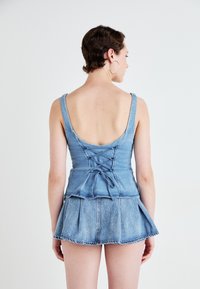 Denim top met een lage rug en vetersluiting, gecombineerd met een uitlopende denim mini rok. Lichtblauwe kleur en zachte textuur.