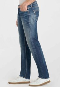 Jeans de mezclilla en un lavado azul medio con un corte recto. Presenta detalles de costura, cinco bolsillos y una cinturilla clásica. Combinados con zapatillas blancas.