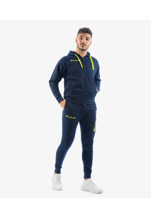 Felpa con zip color navy con dettagli gialli, pantaloni jogger aderenti abbinati e sneakers bianche. Il tessuto sembra morbido, con dettagli del logo visibili sull'abbigliamento.