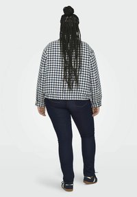 Marynarka w wzór houndstooth w granatowo-białym materiale, o luźnym kroju, długich rękawach i okrągłym dolnym wykończeniu, zestawiona z ciemnymi obcisłymi dżinsami i casualowymi butami.