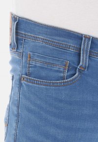 Jeans de denim azul con un lavado claro, costuras visibles, un pequeño bolsillo frontal y un diseño de cintura estándar con una etiqueta de cuero.