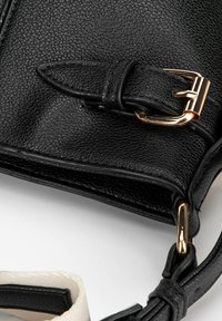 Borsa a tracolla in pelle nera, con superficie testurizzata, fibbia in metallo dorato e attacco della tracolla bianco a contrasto.