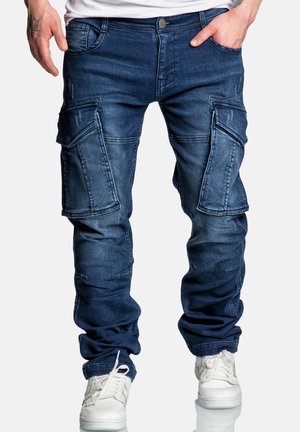 Dunkelblaue Denim-Cargo-Hosen mit mehreren Seitentaschen, Used-Look-Details und schmalem Schnitt, kombiniert mit weißen Sneakers.