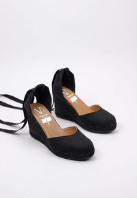 Zapatos de cuña negros de lienzo con puntera redondeada, talón abierto, lazos en el tobillo y una plataforma recubierta de yute texturizado para mayor altura.
