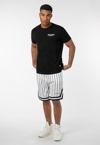 Black short-sleeve t-shirt with white "Urban Edition" text; paired with white striped shorts featuring black accents, and white sneakers.