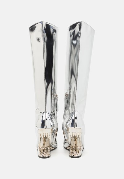 Silver metallic knee-high boots with a sleek surface, rounded toe, and distinctive metallic heel accent shaped like an ornate design.
