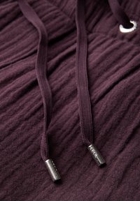 Tissu violet foncé avec une surface texturée, comportant deux cordons de serrage avec des embouts et des œillets en métal argenté pour l'ajustement.