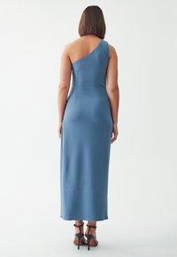 Asymmetrisches blaues Kleid aus glattem Stoff, tailliertem Oberteil und einem langen Rock. Es hat einen einzelnen Träger und ein tief ausgeschnittenes Rückendesign.
