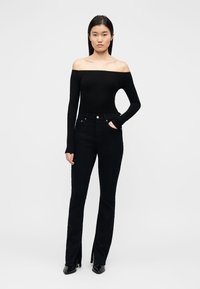 Μαύρο μπλουζάκι με μακριά μανίκια και σκίσιμο στους ώμους και μαύρο τζιν με καμπάνα, ψηλόμεσο με πλευρικές σκισμές, συνδυασμένο με γόβες με μυτερή μύτη.