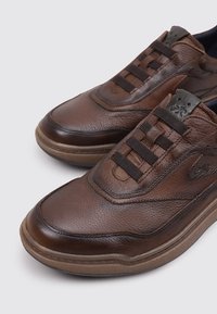 Zapatillas de piel marrón con acabado texturizado, que presentan un diseño sin cordones, suelas de goma y un sutil logo en el lateral.