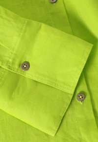 Helles limonengrünes Leinengewebe mit einem Falten- und Knopfdetail, das hölzerne Knöpfe und kontrastierende Nähte aufweist. Glatte Textur.