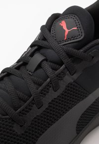 Scarpa sportiva nera realizzata in tessuto testurizzato con accenti lisci, dotata di lacci neri, suola in gomma e logo Puma rosso sulla linguetta.