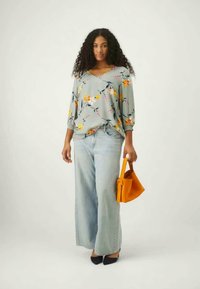 Γκρίζο τοπ με λουλουδάτο σχέδιο και τρία τέταρτα μανίκια, συνδυασμένο με ανοιχτό μπλε παντελόνι σε φαρδιά γραμμή και φωτεινή πορτοκαλί τσάντα. Μαύρες γόβες ολοκληρώνουν την εμφάνιση.