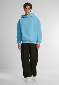 Hoodie azzurro chiaro con tasca frontale, polsini e fondo a coste. Abbinato a pantaloni cargo neri a vestibilità ampia e sneakers bianche.