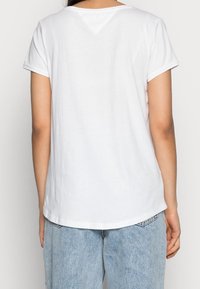 Camiseta de algodón blanca con mangas cortas, escote en forma de V y dobladillo redondeado. Combinada con jeans de mezclilla de color azul claro.