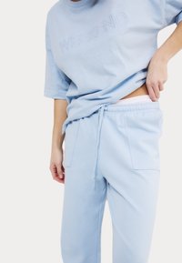 Camiseta de algodón azul clara con la palabra "WEEKEND" bordada en el centro, combinada con pantalones de chándal con cordón a juego que cuentan con dos bolsillos.
