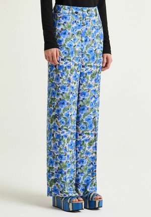 Floral patterned wide-leg trousers in shades of blue and green, made from lightweight fabric, paired with blue platform shoes with striped accents.