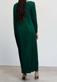 Langes grünes Kleid aus glattem Stoff mit langen Ärmeln und rundem Ausschnitt. Das Design bietet eine lockere Passform und reicht bis zu den Knöcheln.