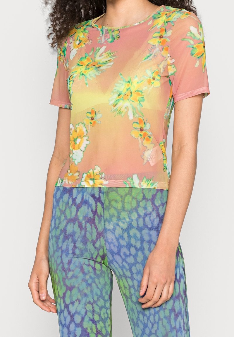 Kortærmet, gennemsigtig bluse med et blomsterprint i pink, gul og grøn. Stoffet har en glat tekstur og en tætsiddende pasform.