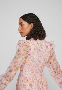 Lys rosa blomsterkjole med volangermarmer, gjennomsiktig stoff og en tettsittende midje. Har en blonderdetalj i midjen og delikate blomster mønstre.