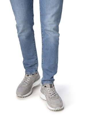 Graue Sneaker aus einer Kombination von Wildleder und Mesh, ausgestattet mit einer weißen Sohle und strukturierten Akzenten, kombiniert mit hellblauen Jeans.