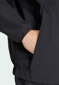 Giacca leggera nera con polsini elasticizzati e tasca laterale visibile, con una texture liscia e orlo regolabile per una vestibilità sicura.