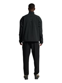 Mann steht mit dem Rücken zugewandt, trägt eine schwarze Jacke mit der Aufschrift "ATW" auf dem oberen Rücken, schwarze Hose und beige-schwarze Sneaker.