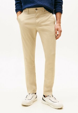 Beige chino's gemaakt van katoenmixstof, met een slim-fit ontwerp, voorzakken en een knoopsluiting. Gemaakt met witte sneakers.