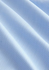 Helles blaues texturiertes Gewebe mit einem subtilen Diamantmuster, das sanfte Falten zeigt und die gewobene Struktur des Materials hervorhebt.