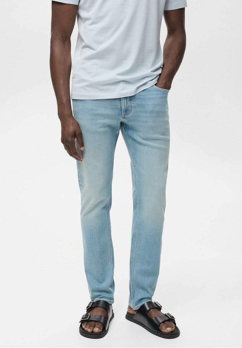 Lichtblauwe denim jeans met een vervaagde afwerking, slim-fit ontwerp en een zachte textuur, gecombineerd met zwarte sandalen en een lichtgrijze t-shirt.