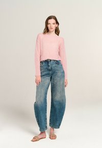 Helles, strukturiertes, langärmliges Oberteil in Rosa, kombiniert mit weit geschnittenen, blauen, ausgewaschenen Jeans. Die Accessoires umfassen beiges, geflochtenes Sandalen. Einfaches, lässiges Ensemble.