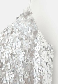 Tessuto di paillettes argento con forme diverse, sovrapposto a una base chiara. La texture riflettente crea un effetto scintillante. Cinghia regolabile visibile.