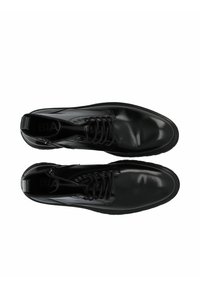 Botas de cuero negro con un acabado pulido, cuentan con cordones y una tira en la parte posterior para tirar. La suela es texturizada y plana con un dibujo mínimo.