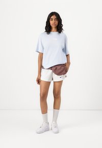 Šviesiai mėlyna marškinėliai trumpomis rankovėmis, balta Nike logotipas, derinama su baltomis šortais ir bordo spalvos juosmens krepšiu, papildyta baltais sportbačiais.