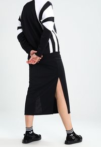 Svart atletisk klänning med en sidoklyfta, kombinerad med svarta sandaler och randiga strumpor. Den övre delen har djärva svartvita ränder på ärmarna.