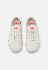 White mesh sneakers with round toes, featuring white laces, a textured upper, and a white speckled rubber sole. Red logo branding inside.