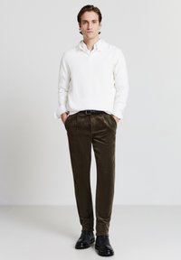 Maglione bianco a coste, pantaloni in corduroy verde oliva, scarpe in pelle nere. Vestibilità slim, colletto alto, con texture evidente e dettagli su misura.